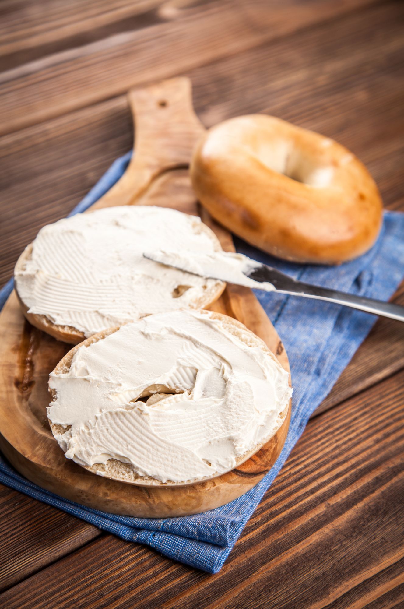 Cream cheese smothered bagels on a cutting board.